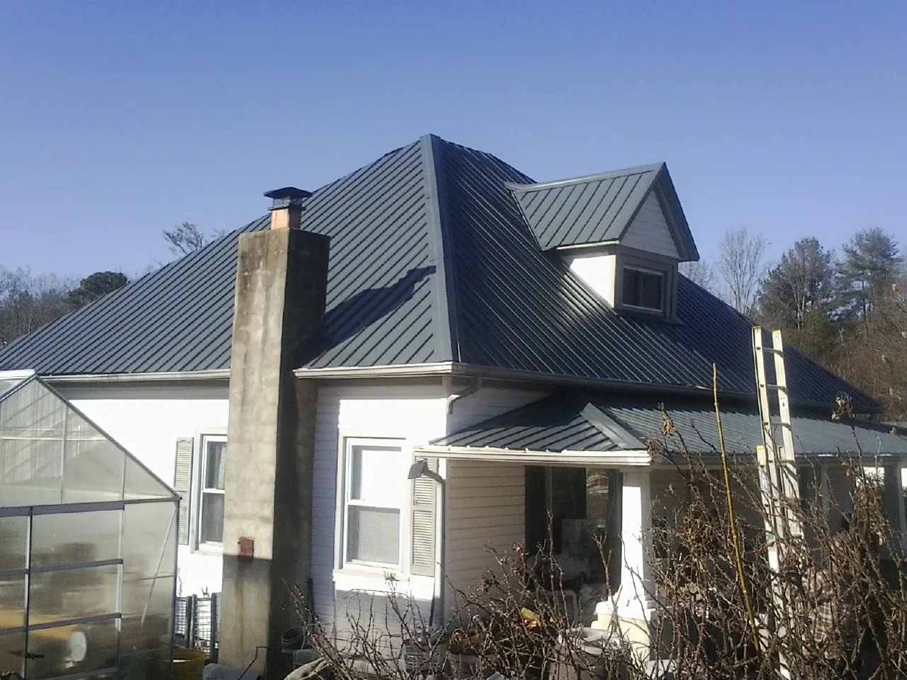 Dark blue standing seam metal roof on a white farmhouse with dormer — Slate & Tile Roof Repair by Roofing Brothers in Durant