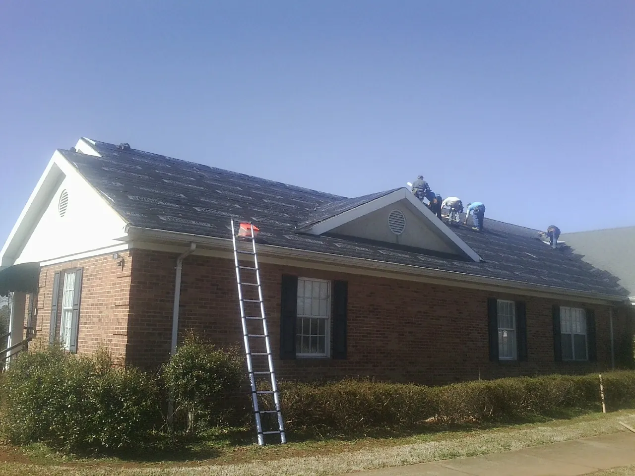 Crew tearing shingles off a brick ranch roof with a ladder set — Emergency Roof Repair work by our crew in Durant