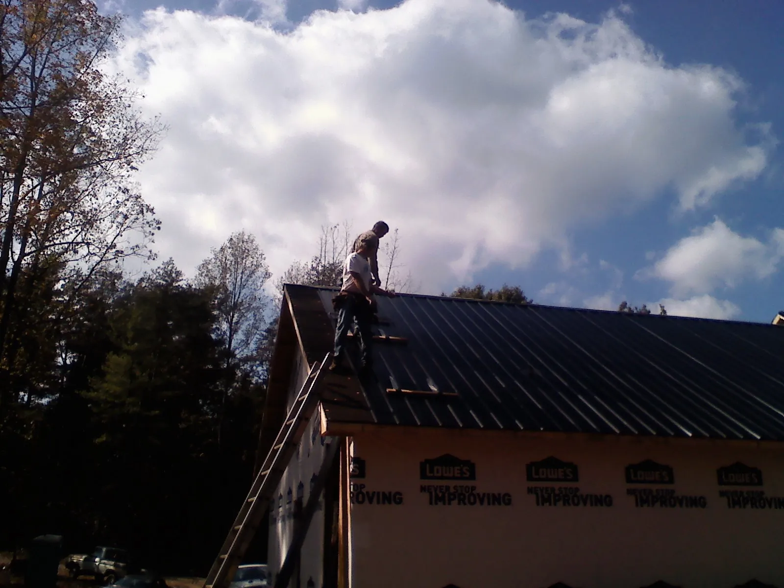 Roofer fastening dark metal panels high against a cloudy sky, from a Roof Inspection job in Durant