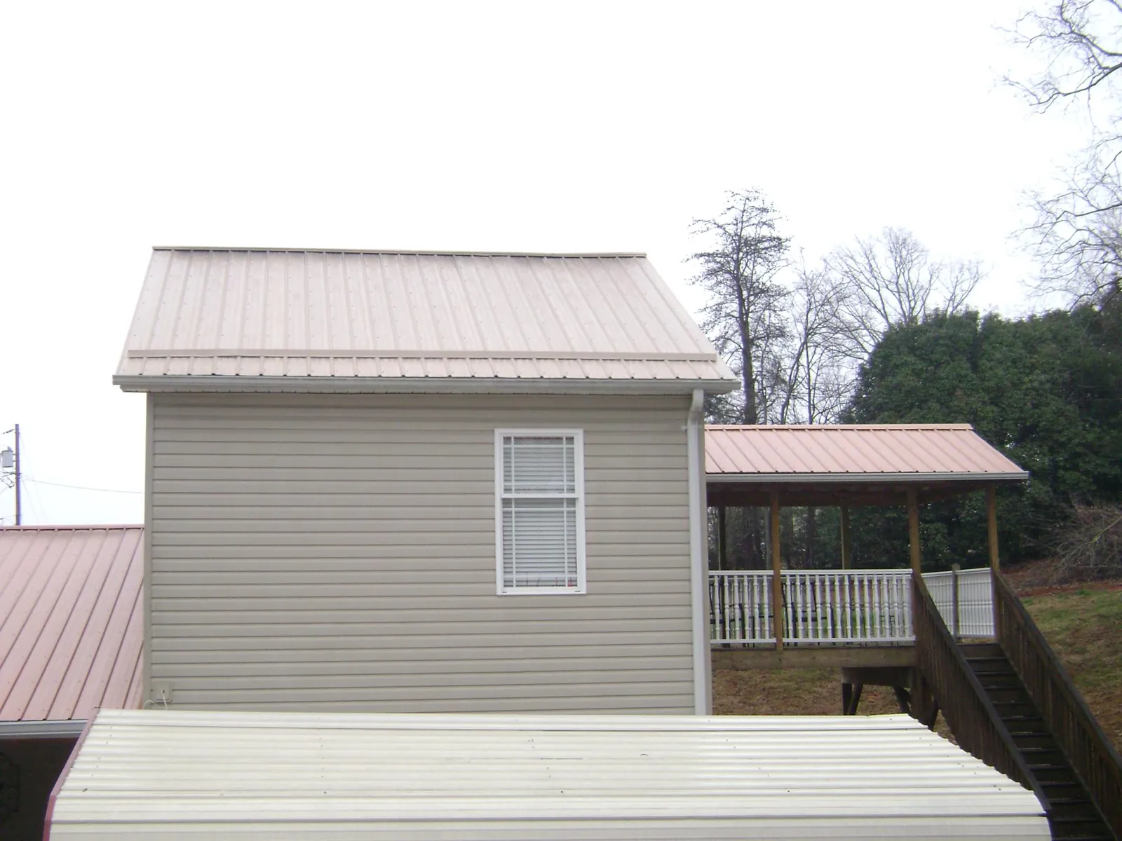 Tan metal roofs on a two story addition and attached porch, from a Roof Replacement job in Durant